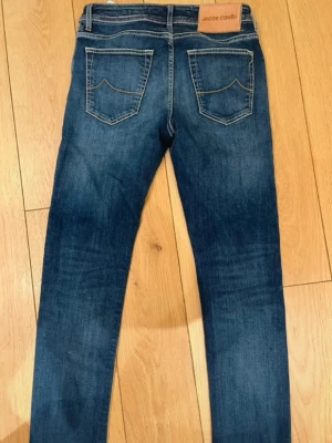 Blå skinny jeans från Jacob Cohën - Snygga blå skinny jeans från Jacob Cohën med klassisk femficksdesign och kontrastsömmar. Jeansen har en mörk tvätt med lätt slitning och patch med logga bak i midjan. Perfekta för en trendig och avslappnad stil.