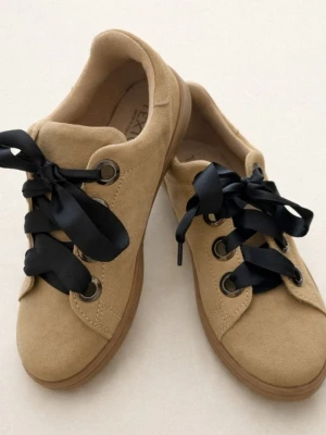 Beige sneakers med svarta band - Snygga beige sneakers i mockaimitation med breda svarta satinband som skosnören. Skorna har rund tå, grova metallöljetter och en klassisk låg siluett. Yttermaterialet är mjukt och ger en stilren look som passar till många outfits.