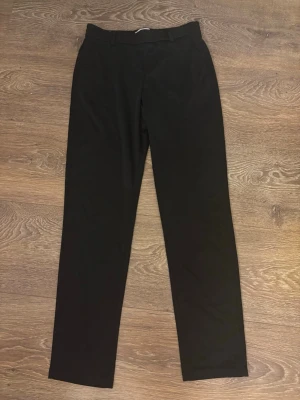Svarta raka kostymbyxor - Snygga svarta kostymbyxor med rak passform och klassiska bälteshällor. Byxorna har en stilren look och passar perfekt till skjorta eller kavaj. Materialet ser ut att vara en mjuk och följsam textil som ger en clean siluett.