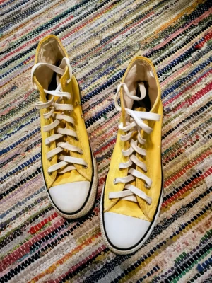 Gula Converse Chuck Taylor Highs - Säljer ett par klassiska Converse Chuck Taylor All Star i gult canvasmaterial med vita gummisulor och tåhättor. Skorna har högt skaft, vita snören och den ikoniska loggan på sidan. Perfekta för dig som vill sticka ut med färg på fötterna.