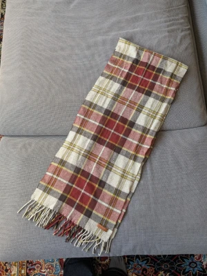 Rutig halsduk från Marlboro Classics - Snygg rutig halsduk från Marlboro Classics i ullmix. Färgerna är vinröd, beige, grå och gul med klassiskt rutmönster och fransar i ändarna. Perfekt accessoar för att lyfta din outfit med en tidlös look.