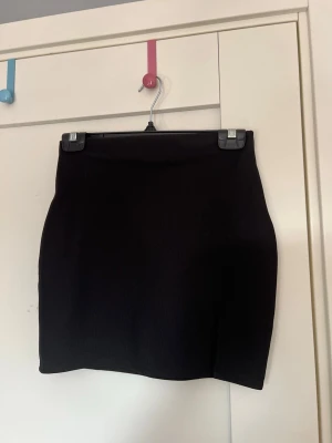 Svart tight kortkjol med slits - Enkel och stilren svart kortkjol med tight passform. Kjolen har en klassisk design med slits, vilket gör den lätt att matcha med olika toppar. Perfekt för dig som gillar minimalistisk stil.