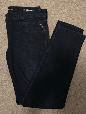 Mörkblå jeans från Replay - Snygga mörkblå jeans från Replay med klassisk femficksmodell och raka ben. Jeansen har diskreta sömmar och en liten Replay-logga vid fickan fram. Tillverkade i mjukt denimtyg som sitter skönt hela dagen.