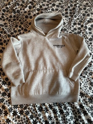 Grå essentials hoodie S - Säljer min stilrena Essentials hoodie från Fear of God i grå färg. Perfekt basic som passar till allt – clean och populär just nu. 	•	Storlek: S (true to size) 	•	Färg: Grå 	•	Skick: Väldigt bra / knappt använd 	•	Passform: Oversized & bekväm  🔥 Trendig hoodie som många letar efter 💯 Äkta 📦 Snabb frakt  Skriv vid frågor eller fler bilder! 