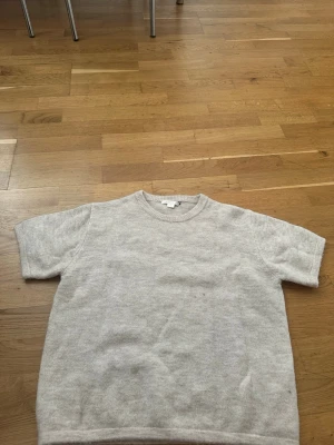 Beige stickad tröja med rund hals - Mysig beige stickad tröja med rund halsringning och korta ärmar. Tröjan har ett litet hål som man ser i bilden.