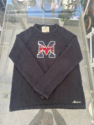 Morris stickad tröja med M-logga – marinblå preppy vibe - Säljer en riktigt clean stickad tröja från Morris 🔥 Marinblå med stor M-logga framtill i UK flagg-design – ger stark preppy / old money vibe.  Storlek L, sitter snyggt och kan även funka lite oversized beroende på passform du vill ha. Lätt att styla med jeans, cargos eller över skjorta för en mer uppklädd look.  Material: 100% bomull – skön och funkar året runt.  Skick: Mycket bra skick, knappt använd och inga synliga defekter.  Perfekt för dig som gillar vintage, preppy fits eller clean street