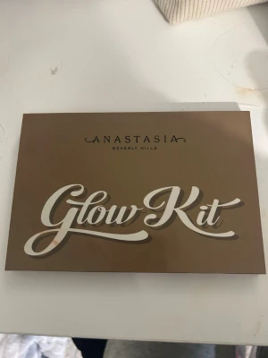Anastasia Glow Kit highlighterpalett - Glow Kit från Anastasia Beverly Hills med sex olika highlighters i nyanserna Snow, White Sand, Golden Dawn, Sunray, Amber Gold och Hot Sand. Paletten har en spegel och kommer i en snygg brun förpackning. Perfekt för att skapa en glowy look.