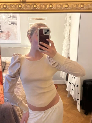 Beige ribbad topp med puffärm - Trendig beige ribbad topp med långa puffärmar och rund halsringning. Snygg croppad passform som ger en modern look. Perfekt att styla med både jeans och kjol för en cool outfit.