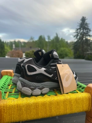 Svarta och grå Asics sneakers - Snygga sneakers från Asics i svart och grått med meshpaneler och detaljer i mocka. Skorna har en chunky sula och klassisk Asics-logga på sidan. Perfekta för dig som gillar sportig och trendig stil.