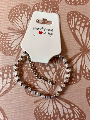 Handgjort pärlarmband i silver och vitt - Snyggt handgjort armband med vita och silvriga pärlor på en tunn kedja. Armbandet har justerbar längd med en liten kedja och lås. Perfekt accessoar för att lyfta din stil med en personlig touch.