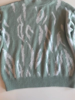 Mintgrön stickad tröja från NA-KD - Snygg mintgrön  stickad tröja från NA-KD med vitt abstrakt mönster. Tröjan har ribbstickad hals, ärmslut och nederkant. Perfekt för dig som gillar trendiga och bekväma plagg med lite extra attityd.