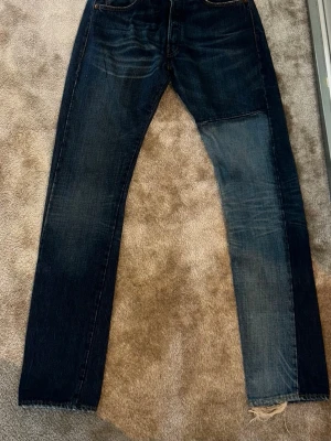 Mörkblå Levi's jeans med patch - Säljer ett par mörkblå Levi's jeans med klassisk femficksdesign. Jeansen har en ljusare patch på höger ben och slitna detaljer vid benslutet. Raka ben och tydliga sömmar. Perfekta för en avslappnad streetstil. W 34 L 36, små i storlek 