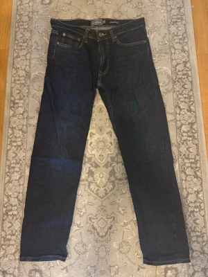 Mörkblå raka jeans - Snygga mörkblå jeans med raka ben och klassisk femficksdesign. Jeansen har kontrastsömmar och en läderpatch bak i midjan. Perfekta för en stilren och enkel look. Materialet är denim i bomull. Nästan aldrig använd, från Dressman storlek