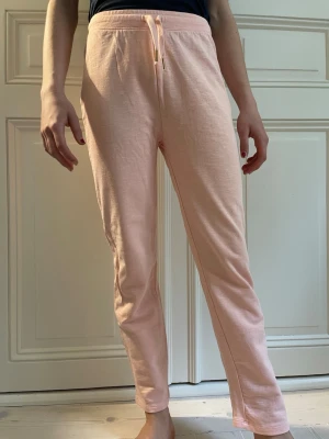 Ljusrosa mjuka loungewearbyxor - Superbekväma ljusrosa loungewearbyxor med dragsko i midjan och en bakficka. Byxorna är raka i modellen och tillverkade i ett mjukt, stretchigt material som passar perfekt för hemmamys eller chill dagar.
