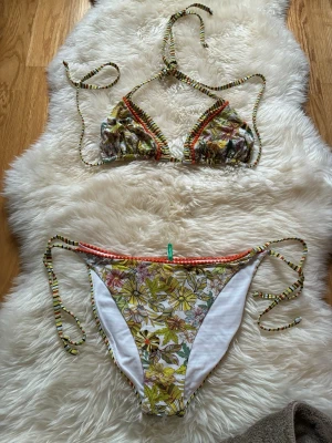 Palmers Blommig och randig bikini med knyt - Snygg bikini från OAS med blommigt mönster på ena sidan och färgglada ränder på andra. Både överdel och underdel har knytband och fina detaljer i orange, grönt och gult. Perfekt för stranden eller poolen!