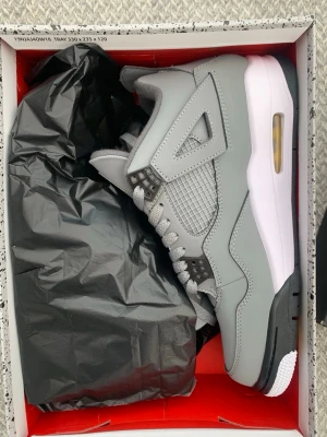 Air Jordan 4 Retro Cool Grey - Snygga Air Jordan 4 Retro Cool Grey sneakers med grå ovandel i läder och mesh, vita och svarta detaljer samt synlig Air-enhet i sulan. Klassisk Jumpman-logga och ikonisk siluett som sticker ut. Perfekta för dig som vill ha stilrena och trendiga sneakers.