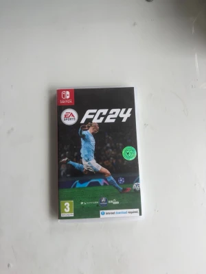 Nintendo Switch spel EA Sports FC24 - EA Sports FC24 till Nintendo Switch, fotbollsspel med svart och grön omslagsdesign. Spelet levereras i plastfodral med spelkassett och informationsblad. Perfekt för dig som gillar sport och gaming.