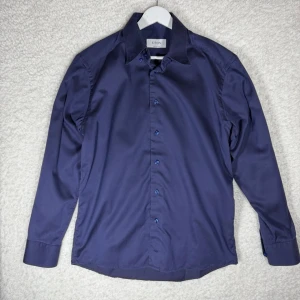 Marinblå skjorta från Eton custom made  - Snygg mörkblå skjorta från Eton med klassisk krage och knappar framtill. Skjortan har lång ärm och är tillverkad i ett slätt tyg som ger en stilren look. Perfekt för dig som gillar stilrena och tidlösa plagg.