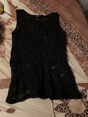 Svart spetsklänning ärmlös - Snygg svart ärmlös klänning med spetsdetaljer och rund halsringning. Klänningen har en kort längd och ett feminint fall nertill. Perfekt för dig som gillar en klassisk och stilren look.