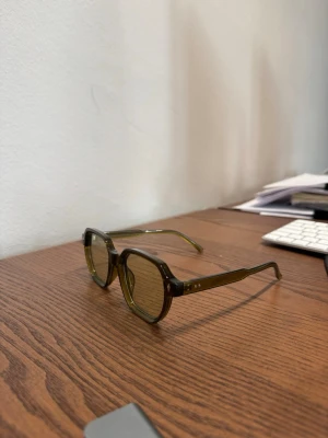 Olivgröna retro solglasögon - Snygga solglasögon med olivgröna, fyrkantiga bågar och tonade glas. Modellen har en cool retrostil med markerade kanter och transparent plastmaterial. Perfekta för dig som vill sticka ut med en unik accessoar.