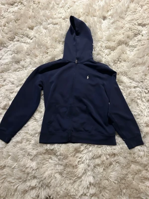 Mörkblå hoodie från Polo Ralph Lauren - Marinblå hoodie från Ralph lauren, den är väldigt snygg och stilig och funkar till allt men säljer då jag inte använder 