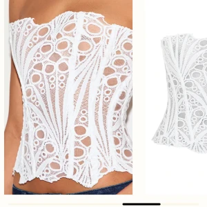 Vit spetskorsett med snörning - Trendig vit korsettopp i spets med unikt mönster och transparenta partier. Toppen är axelbandslös och har snygg snörning i ryggen för justerbar passform. Perfekt att styla med jeans eller kjol för en cool look.
