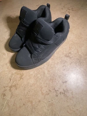 Svarta DC Shoes sneakers - PRIS KAN DISKUTERAS Säljer ett par helsvarta DC Shoes sneakers i storlek 39 med klassisk låg profil och tjock vadderad plös. Skorna har en robust gummisula, diskret DC-logga på sidan och är tillverkade i syntetmaterial med textilfoder. Perfekta för dig som gillar streetwear och skate-inspirerad stil. Kan även passa folk med storlek 40, möjligtvis 41.