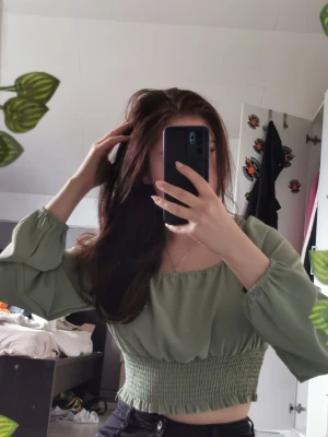 Grön croppad blus med puffärm - Snygg ljusgrön croppad blus med långa puffärmar och smockad midja. Toppen har en fyrkantig ringning och är perfekt för dig som gillar trendiga och bekväma plagg. Passar till både jeans och kjol.