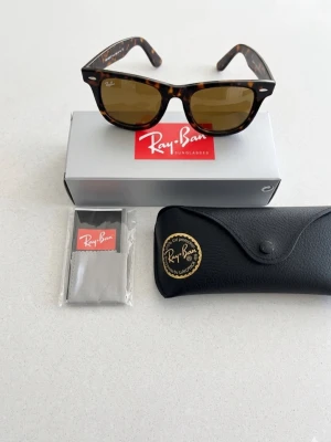 Ray-Ban Wayfarer solglasögon brun - Ray-Ban Wayfarer solglasögon med brunmelerad båge och bruna glas. Klassisk och tidlös design med Ray-Ban-logga på linsen. Medföljer originalfodral och putsduk. Perfekt för dig som vill ha en ikonisk look.