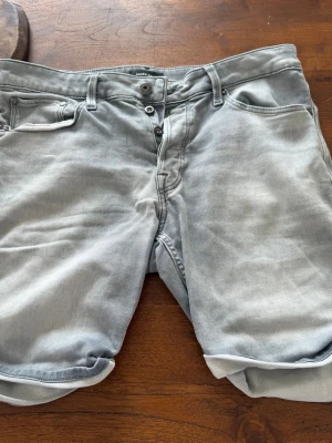 Ljusgrå jeansshorts med knappar - SÄLJER ETT TILL PAR FAST LJUSBLÅA FRÅN JACK&JONES, ST PRIS 149kr BÅDA 249kr!!Säljer ett par ljusgrå jeansshorts med knappgylf och uppvikta benslut. Klassisk femficksmodell med bakfickor och bälteshällor. Perfekta för dig som gillar en avslappnad stil.