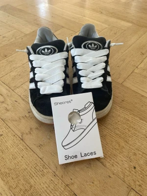 Adidas Campus 00s Svart/Vit - Säljer ett par riktigt snygga Adidas Campus 00s i den klassiska svartvita färgställningen. Perfekta sneakers med den rätta, feta skate-looken! Jag har nyss bytt ut de gamla snören till helt nya snören. Man får också med ett par extra nya skosnöre.