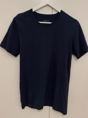 Mörkblå t-shirt från BOSS - Snygg mörkblå t-shirt från BOSS med diskret logga på bröstet. Klassisk rund halsringning och korta ärmar. Perfekt basplagg i mjuk bomull som passar till allt. Enkel och stilren design för en clean look.