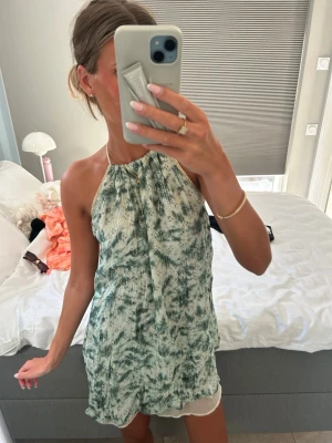 Ibiza mini klänning - Halterneck klänning som är perfekt till stranden eller att klä upp med ett par klackar utomlands. Glittrig och har fina detaljer längst halsen och banden där bak där man knyter åt. Fint skick! Kortare där fram än bak.