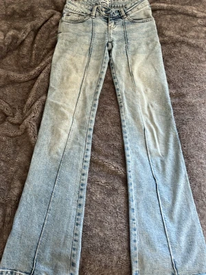 Ljusblå utsvängda jeans med söm - Säljer ett par ljusblå jeans med utsvängda ben och markerade sömmar framtill. Jeansen har låg midja. Tyvärr har de några enstaka fläckar som tyvärr inte går bort, men de syns knappt, inget man tänker på.