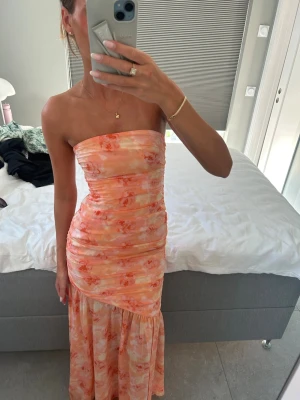 Adoore klänning - Orange/peach bandeau klänning från Adoore. Den är helt slutsåld. Endast använd under en fest så de är nyskick. Storlek 32, funkar för mig som brukar ha 34 i adoores klänningar med.