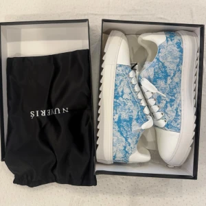 Vita och blå Numeris sneakers med mönster - Snygga sneakers i vitt och blått med unikt mönster och vita snören. Skorna har en låg siluett och grov sula med taggig kant. Ovandelen är i textil och läderimitation, perfekt för dig som vill sticka ut med din stil.