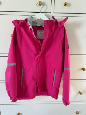 Polarn o pyret vindjacka  - Rosa vindjacka från polarn o pyret. Jackan har reflexdetaljer på ärmar och fickor samt två framfickor med dragkedja. Sparsamt använd  av 1 barn. Strl 134.