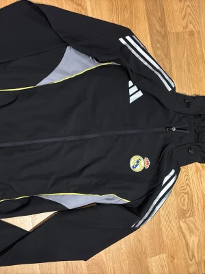 Adidas  realmadrid träningsset - Komplett träningsset från Real Madrids kollektion. Innehåller [Jacka/Tröja] och matchande träningsbyxor. Perfekt för både träning på hög nivå eller en sportig streetwear-look. 
