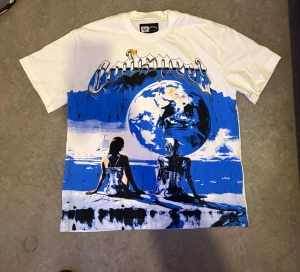 Vit t-shirt med blått tryck och motiv - Unik vit t-shirt med stort blått och svart tryck framtill som visar två figurer vid en stor jordglob. Texten 'E Pluribus Unum' och grafiska detaljer på baksidan. Oversized passform och coolt, futuristiskt motiv. Perfekt för dig som gillar streetwear och statement-plagg.