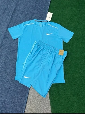 Blått träningsset från Nike - Snyggt blått träningsset från Nike med matchande t-shirt och shorts. Båda plaggen har den klassiska vita Nike-loggan och är tillverkade i ett lätt och snabbtorkande material som passar perfekt för träning eller sportaktiviteter.