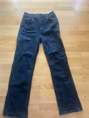 Svarta high waist raka jeans - Säljer ett par svarta jeans med hög midja och raka ben. Klassisk femficksmodell med dragkedja och knapp framtill. Jeansen har bredare passform och är perfekta för en avslappnad stil. Materialet är denim i bomull.