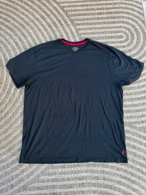 Svart t-shirt från Polo Ralph Lauren supreme quality  - Klassisk svart t-shirt från Polo Ralph Lauren med röd logga broderad längst ner. T-shirten har rund halsringning och korta ärmar. Tillverkad i mjuk bomull och har en clean, stilren look med en liten färgdetalj i nacken.