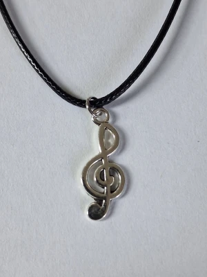 Halsband med silverfärgad G-klav/nota - Vaxat läderhalsband och ett silverfärgat hänge i form av en G-klav/nota Perfekt för dig som älskar musik och vill ha en unik detalj till din stil. Materialet är rostfritt stål på notan