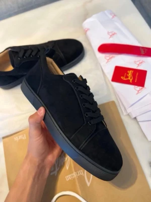 Svarta sneakers från Christian Louboutin - Stilrena svarta sneakers från Christian Louboutin i mocka med matchande svarta skosnören och sula. Klassisk låg modell med rund tå och diskreta sömmar. Insidan är ljusbeige för en snygg kontrast. Perfekta för dig som gillar exklusiv och minimalistisk stil. Använt ett par gånger! 