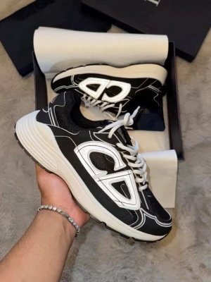 Svarta och vita sneakers med stor logga - Stilrena sneakers i svart och vitt med en stor, reflekterande logga på sidan. Skorna har vita snören, tjock vit sula och detaljer i mesh och syntetmaterial. Perfekta för dig som gillar en sportig och trendig look.