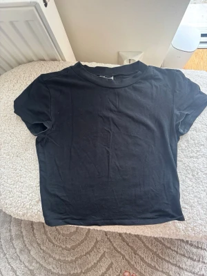 Svart t-shirt från Divided H&M - En enkel svart t-shirt från Divided med klassisk rund hals och korta ärmar. Modellen är rak och passar perfekt till jeans eller kjol. Tillverkad i mjuk bomull för en skön känsla hela dagen.