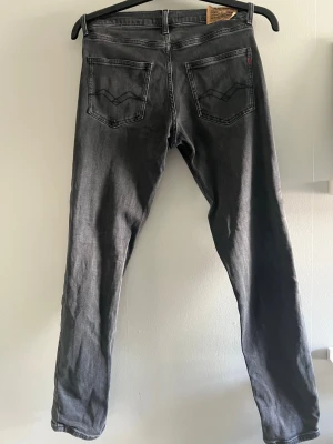 Svarta slim fit jeans från Replay - Snygga svarta slim fit jeans från Replay med klassisk femficksdesign och diskreta slitningar. Jeansen har raka ben och normal midja, perfekta för en trendig och avslappnad look. Materialet är mjukt och stretchigt för extra komfort.