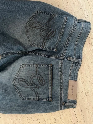 Blå raka jeans från Gant - Säljer ett par klassiska blå jeans från Gant med raka ben och snygga broderade detaljer på bakfickorna. .