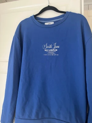 Blå sweatshirt från Sixth June - Blå sweatshirt från Sixth June med vit text på bröstet där det står 'Self Love Club'. Tröjan har rund halsringning och är tillverkad i mjukt material. Perfekt för en avslappnad och trendig stil.
