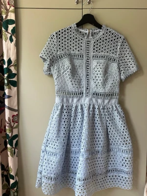 Ljusblå kort klänning från By Malina  - Superfin ljusblå kortklänning med genombruten spets och rund hals. Klänningen har korta ärmar, markerad midja och dragkedja bak. Perfekt för sommarens alla tillfällen och ger en fräsch och trendig look.